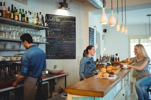 Glückliches barista, das mit Kunden an der Cafeteria sich verständigt