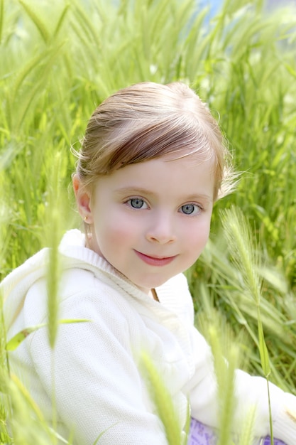 Glückliches blondes kleines Mädchen sitzen auf grüner Spitzenwiese