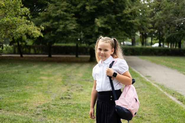 Glückliches blondes lockiges Schulmädchen in Schuluniform mit rosa Rucksack zurück zur Schule im Freien