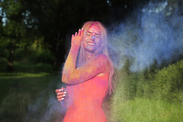 Glückliches blondes Model posiert in einer Wolke aus trockener Farbe beim Holi-Festival