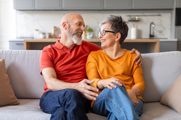 Glückliches Eheporträt von lächelnden älteren Ehepartnern, die sich zu Hause auf der Couch umarmen