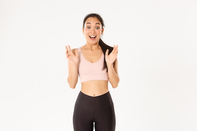 Glückliches enthusiastisches Fitness-Mädchen, asiatische Sportlerin fasst Hände von fantastischen Nachrichten, schnappt erstaunt nach Luft und steht über