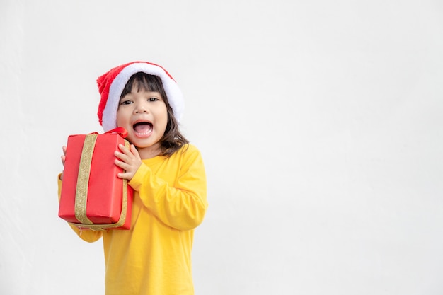 Glückliches entzückendes asiatisches Kindermädchen mit Weihnachtsgeschenk in den Händen auf weißem Hintergrund