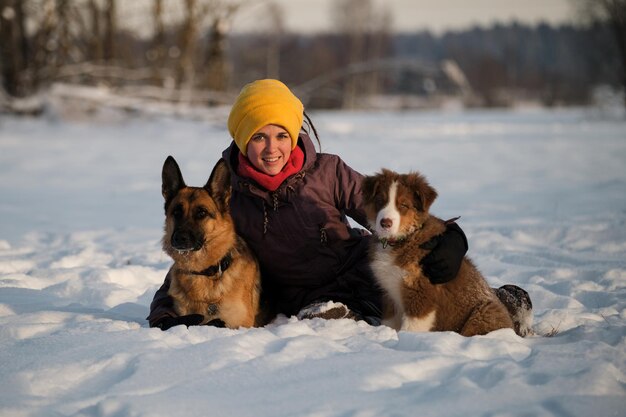 Glückliches europäisches Mädchen auf Spaziergang im Winterpark mit zwei reinrassigen Hunden sitzt im Schnee