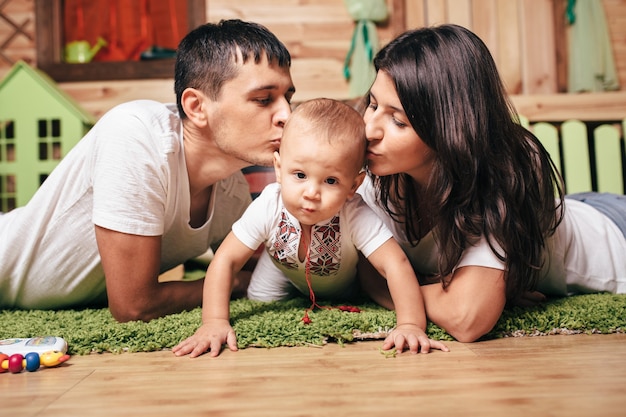 Glückliches Familienporträt, Konzeptliebe eines Familienurlaubs. Mama, Papa küssen Kinderjungen zu Hause auf einer Etage. Gefühle des Glücks. Frauentag. Muttertag, Vatertag.