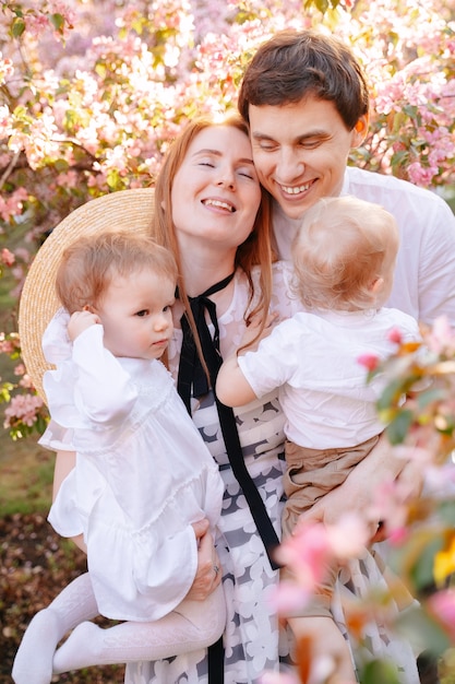 Glückliches Familienporträt von Eltern mit Kindern eines blühenden rosa Apfelbaums im Park lächelnde Mama und Papa umarmen ihre Kinder bei einem Spaziergang im Park in