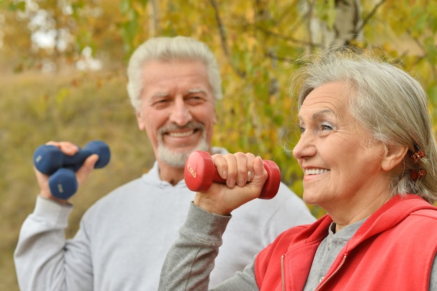 Glückliches fittes älteres Paar, das mit Hanteln im Herbstpark trainiert