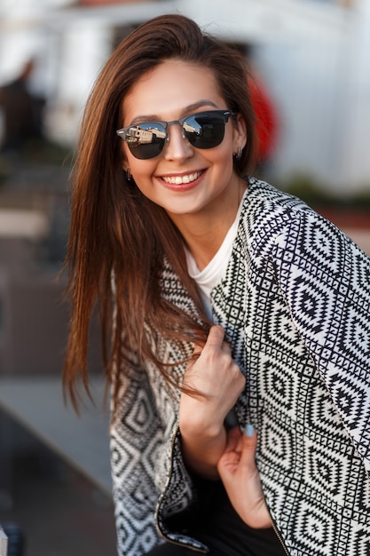 Glückliches Frauenmodell mit einem Lächeln mit modischer Sonnenbrille in einem Café in der Stadt