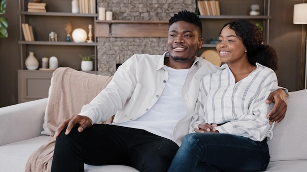 Glückliches frisch verheiratetes Paar heiratete einen afrikanischen Mann und eine Frau, die zu Hause auf dem Sofa sitzen und fernsehen und reden