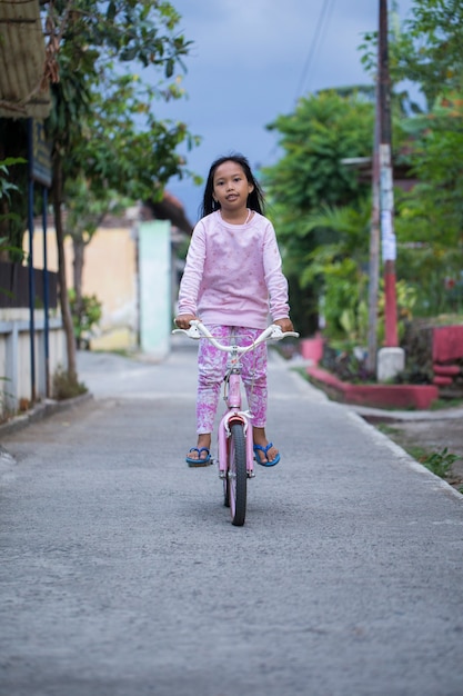 Glückliches fröhliches asiatisches Kindermädchen, das Fahrrad fährt