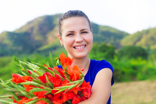 Glückliches fröhliches positives Mädchen, junge hübsche nette Frau lächelnd, lachend mit Feiertagsgeschenk, großer schöner roter Strauß von Gladiolen, Gladiolen. Frühling, 8. März Internationales Frauentagskonzept