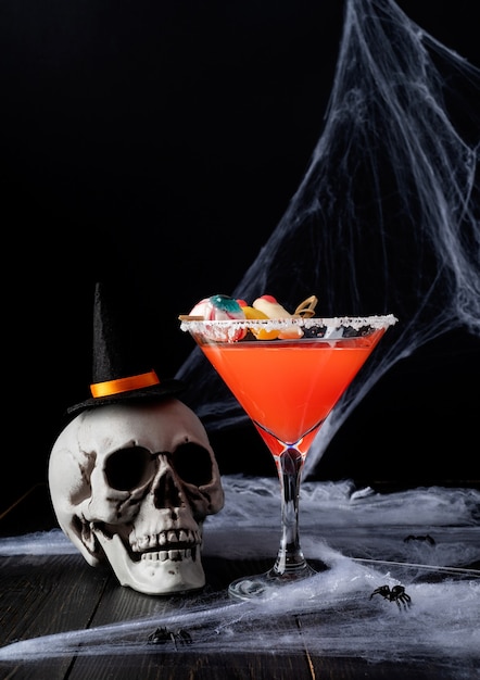 Glückliches Halloween-Konzept. Gruseliger bunter Halloween-Cocktail mit Partydekorationen auf dunklem Hintergrund mit Spinnennetz mit Kopierraum