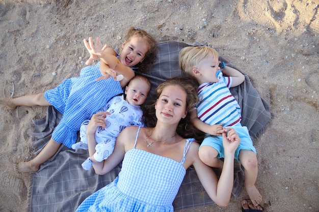 Glückliches harmonisches Familienkonzept im Freien Mutter und drei Kinder liegen auf einer Decke im Sand