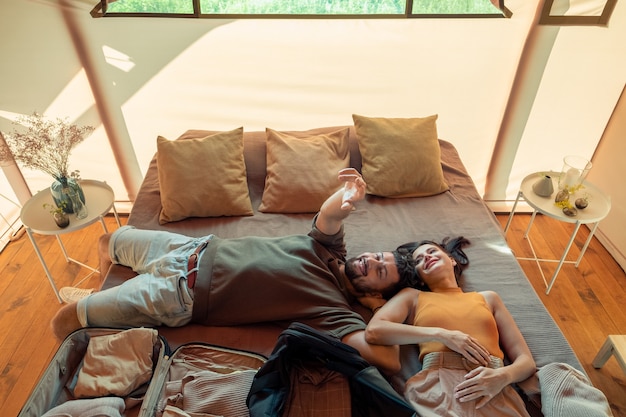 Glückliches idyllisches Paar, das sich auf großem Bett im Glamping-Haus entspannt