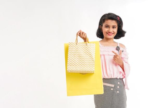 Glückliches indisches kleines Mädchen, das Einkaufstaschen auf weißem Hintergrund hält