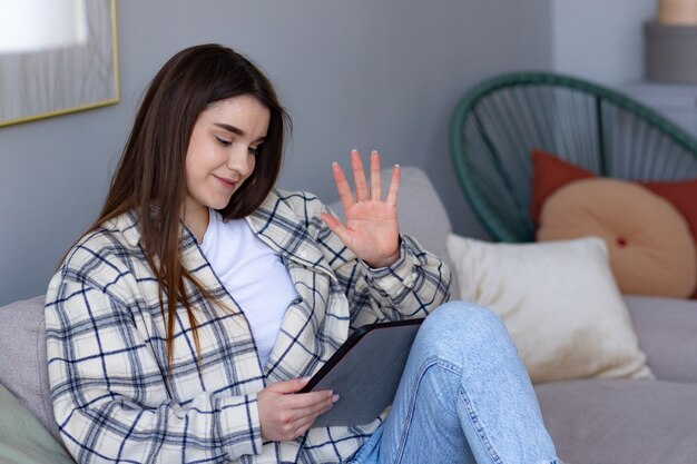 Glückliches jugendlich Mädchen, das Handvideokonferenz winkt, die auf Tablet-Computer anruft, sitzen auf Trainer