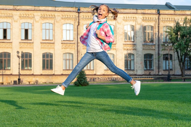 Glückliches jugendlich Mädchen, das im Schulhof draußen zurück zur Schule springt