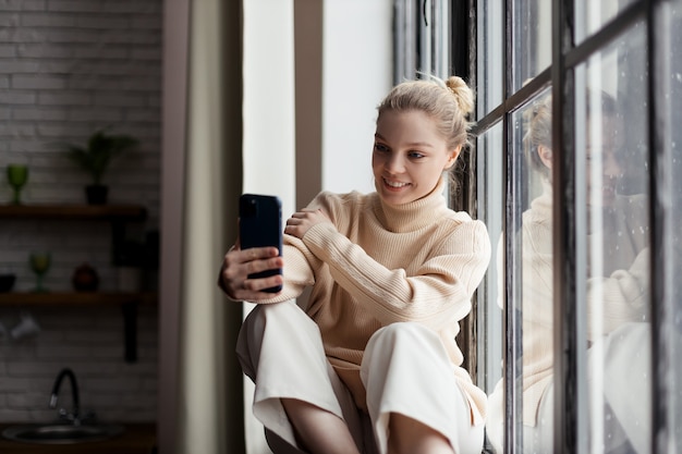 Glückliches jugendlich Mädchen, das soziales Medien hält Smartphone zu Hause hält. Mit dem Handy online einkaufen, Lieferung bestellen. Hochwertiges Foto