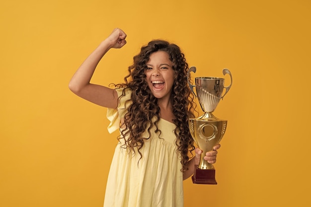 Glückliches jugendlich Mädchen halten goldenen Cup-Leistungspreis, der Erfolg und Sieg feiert