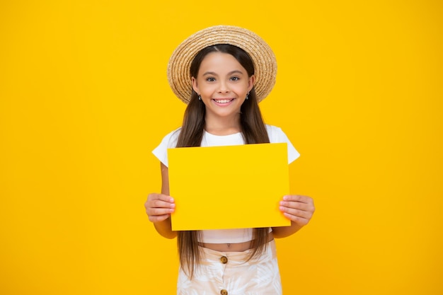 Glückliches jugendlich Mädchen halten leeres Anzeigenpapier mit Kopienraum auf gelbem Hintergrund