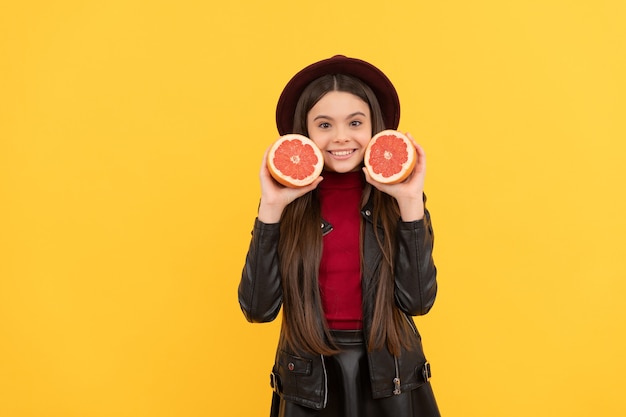 Glückliches jugendlich Mädchen in Hut und Lederjacke halten geschnittene Grapefruit, Diät.