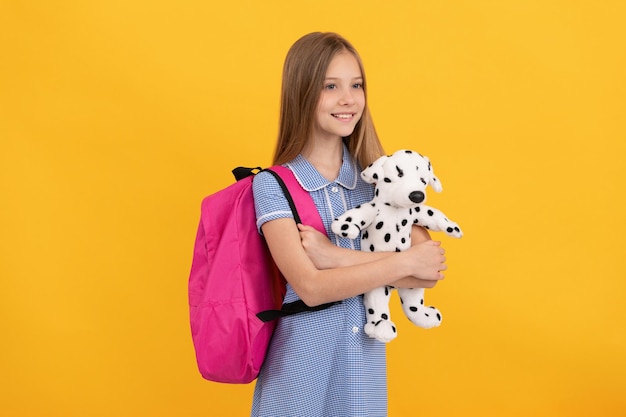 Glückliches jugendlich Mädchen mit Schulrucksack und Spielzeughund, Kindheit.