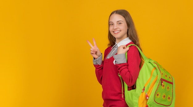 Glückliches jugendlich Mädchen tragen Rucksack. zurück zur Schule. Tag des Wissens. Konzept der Bildung. Kind mit Friedensgeste auf gelbem Hintergrund. 1. september glückliche kindheit. Kind mit Schultasche. Platz kopieren.