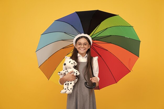 Glückliches jugendlich Mädchen unter buntem Regenschirm in der Herbstsaison halten Spielzeugkindheitsglück