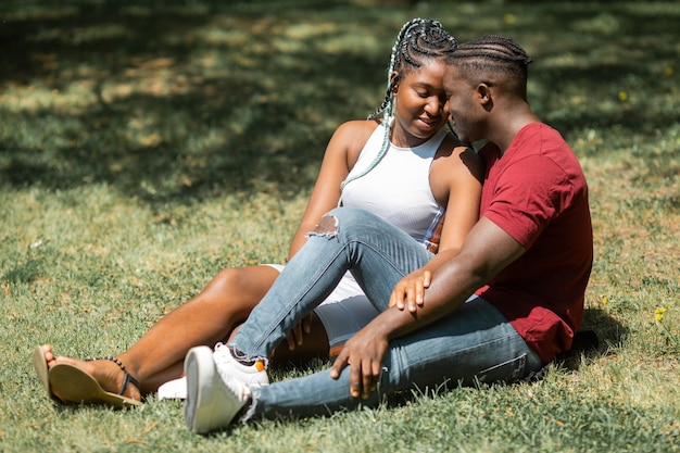 glückliches junges afrikanisches Paar, das im Park auf dem Gras sitzt