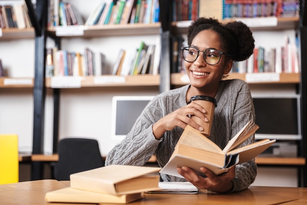 Glückliches junges afrikanisches Studentenmädchen, das an der Bibliothek studiert und ein Buch liest