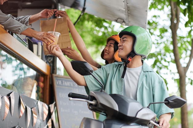 Glückliches junges asiatisches Paar, das eine Papiertüte mit Fast Food und einem Glas Limonade nimmt