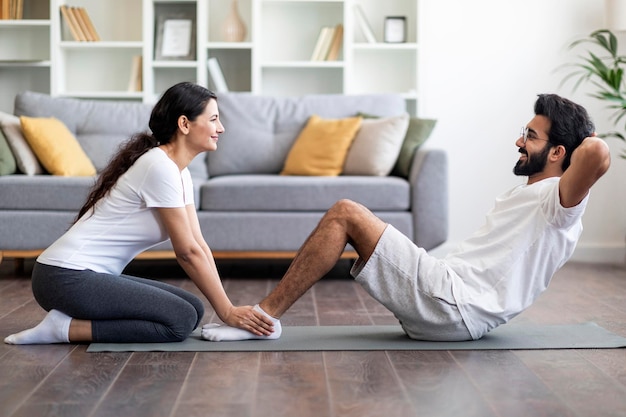 Glückliches junges indisches Paar, das zu Hause gemeinsam Sit-ups macht