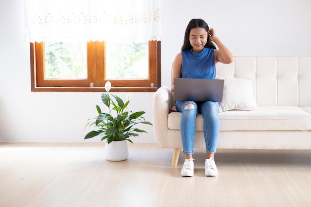 Glückliches junges Mädchen benutzt Computer-Laptop, der zu Hause auf dem Sofa sitzt