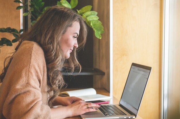 Glückliches junges Mädchen, das an einem Kaffeehaus mit einem Laptop arbeitet