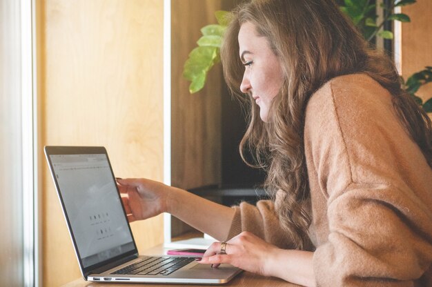 Glückliches junges Mädchen, das an einem Kaffeehaus mit einem Laptop arbeitet