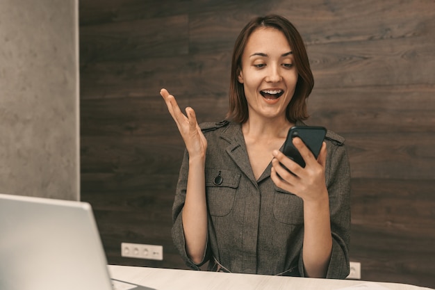 Glückliches junges Mädchen, das auf das Telefon schaut und sich freut