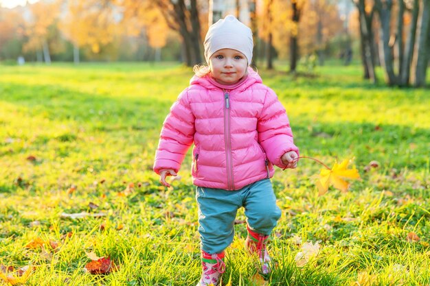 Glückliches junges Mädchen, das im schönen Herbstpark auf Naturspaziergängen im Freien lächelt. Kleines Kind, das mit fallendem gelbem Ahornblatt im orange gelben Hintergrund des Herbstes spielt. Hallo Herbstkonzept.