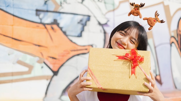 Glückliches junges Mädchen hält die Geschenkbox auf buntem Hintergrund. Asiatisches junges Mädchen.