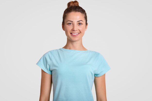 glückliches junges Mädchen mit zahnigem Lächeln, entzücktem Ausdruck, trägt lässiges T-Shirt, ist gut gelaunt, hat gesunde Haut, isoliert über Weiß. Positives Emotionskonzept.