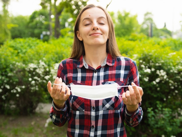 Glückliches junges Mädchen nimmt eine medizinische Maske ab und atmet frische Luft in der Natur