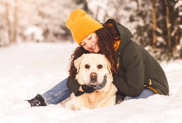 Glückliches junges mädchen umarmt ihren weißen labrador-hund im winter draußen