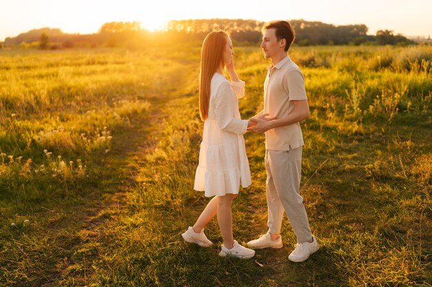 Glückliches junges Paar, das am Sommerabend bei goldenem Sonnenuntergang mit warmem Sonnenlicht auf einer schönen grünen Wiese umarmt und küsst