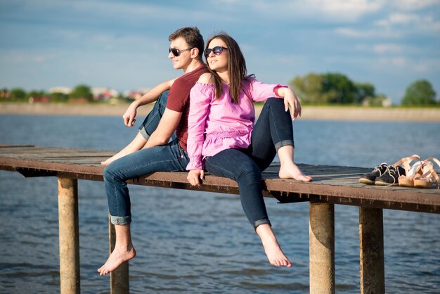 Glückliches junges Paar, das an einem sonnigen Sommertag auf dem Pier am See spazieren geht