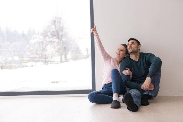 glückliches junges paar, das an kalten wintertagen zu hause in der nähe des fensters sitzt