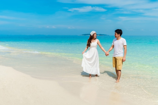 Glückliches junges Paar, das auf dem Meeresstrand bei Koh MunNork Island, Rayong, Thailand geht