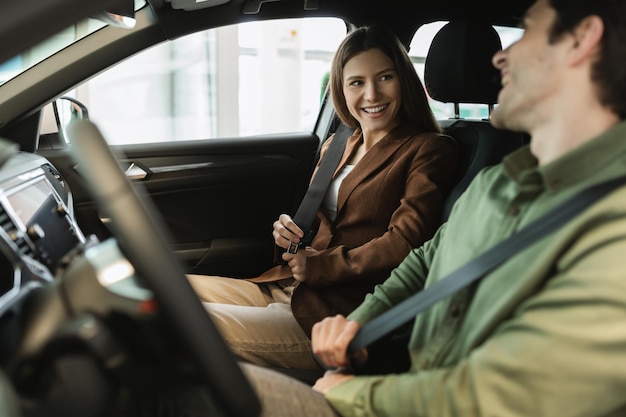 Glückliches junges Paar, das im Automobilsalon sitzt, zufrieden mit der Probefahrt, die den Kauf von neuen bespricht