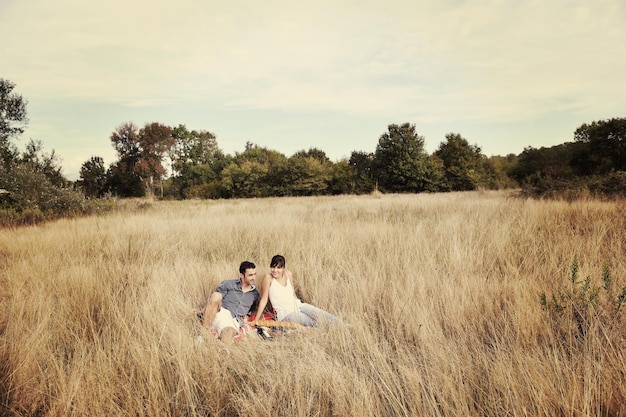 glückliches junges paar, das picknick auf dem land auf dem feld genießt und eine gute zeit hat