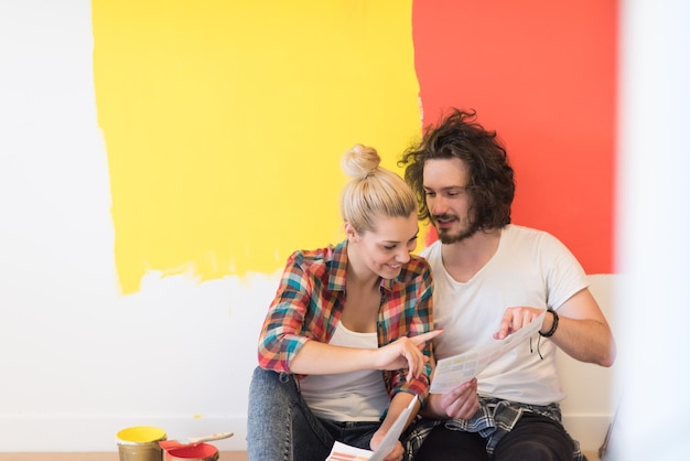 Glückliches junges Paar, das sich entspannt, nachdem es ein Zimmer in seinem neuen Haus auf dem Boden gestrichen hat