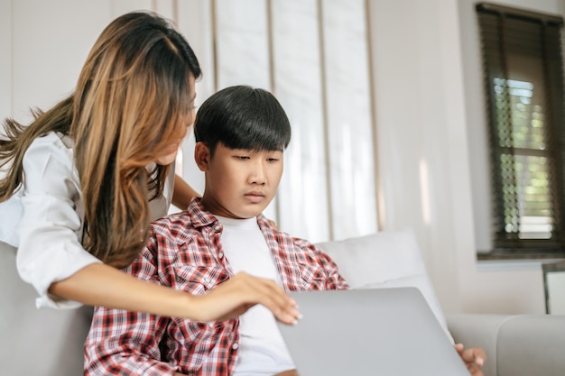 Glückliches junges Paar, das zu Hause auf dem Sofa im Wohnzimmer sitzt, verwendet einen Laptop-Computer, der redet und lächelt zusammen mit dem glücklichen Familienkonzept des Glücks