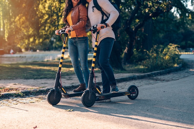 Foto glückliches junges paar, das zusammen beim fahren von elektrorollern im stadtpark genießt.